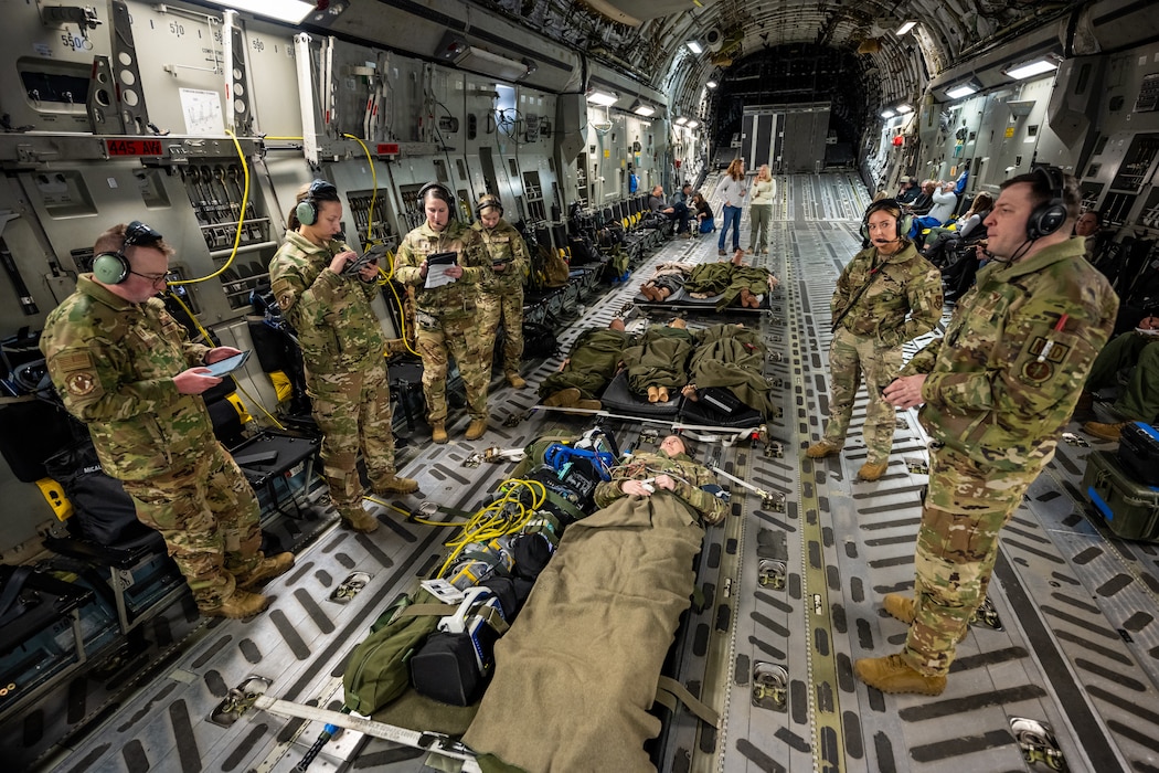 Seven military members stand around strapped down stretchers with another military member playing a mock patient