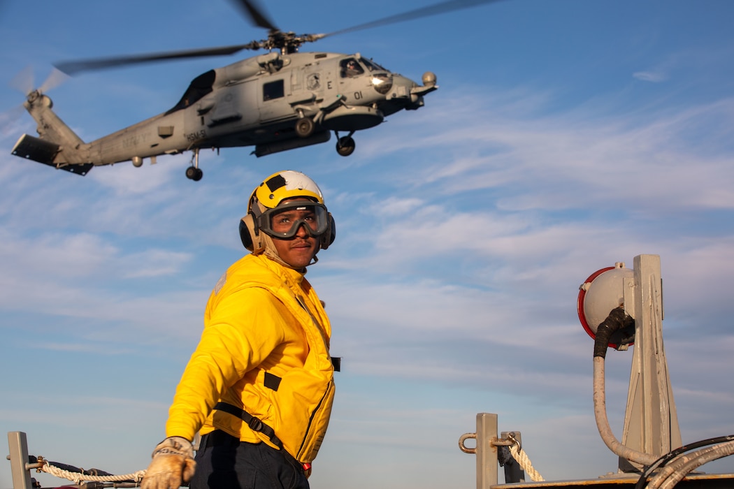 BMSN Rohan Preston signals the pilots of an MH-60R Sea Hawk helicopter from HSM-51 on the flight deck while operating in the Philippine Sea.