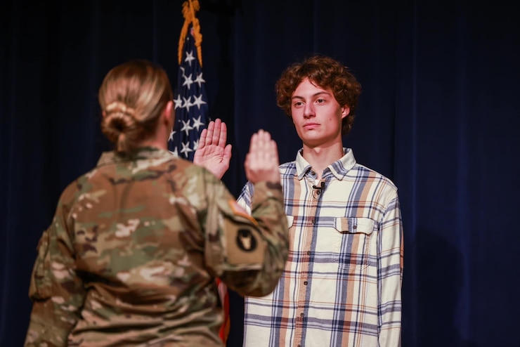 photo of the back of a female soldier with her right arm raised at the elbow and the front of a man with medium curly hair and plaid shirt, his right arm raised at the elbow.