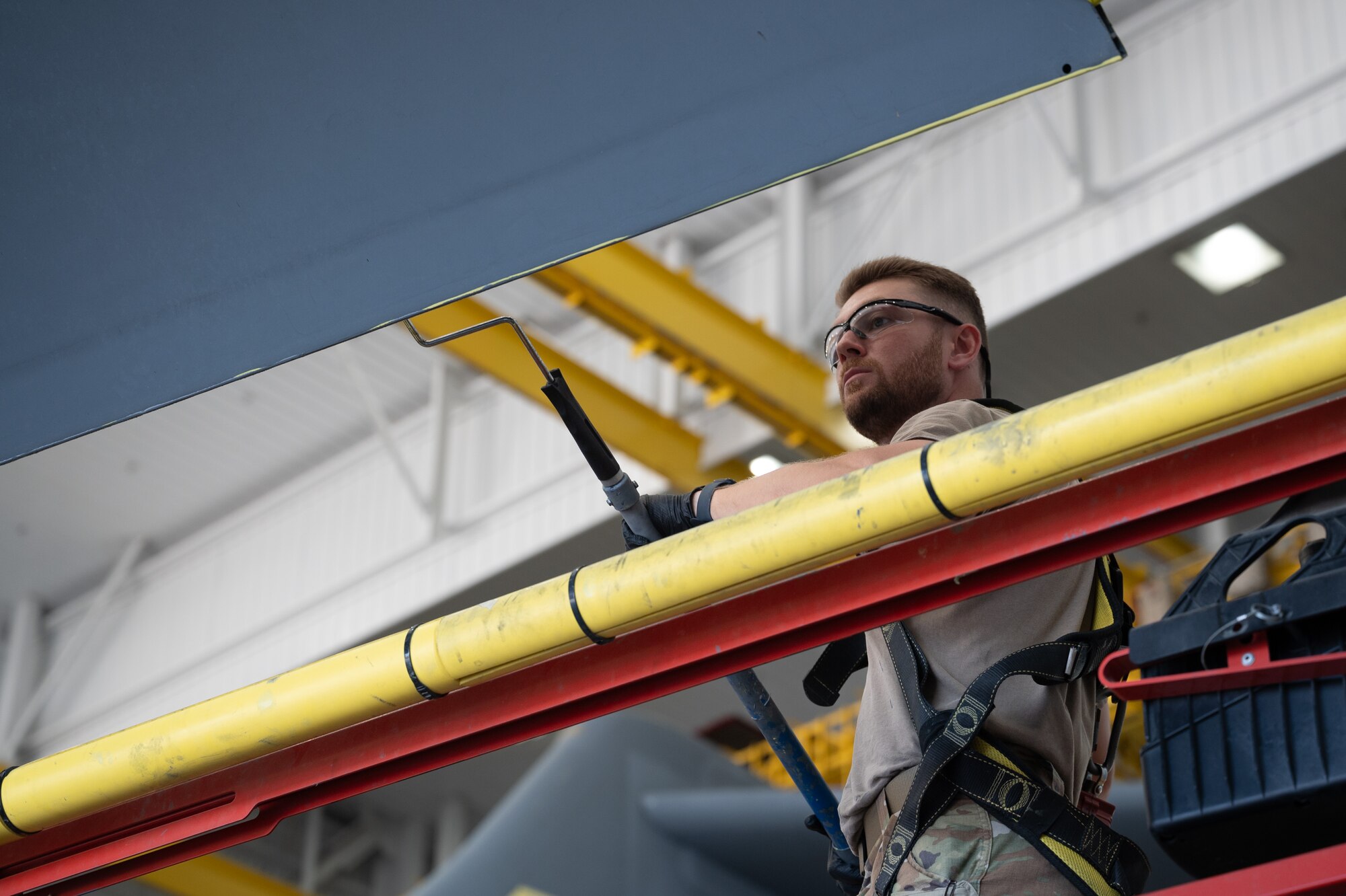 Airman uses paint rolller on a C-17 Globemaster III aircraft wing.