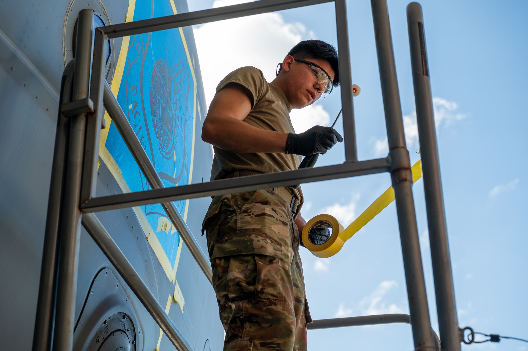 Airman uses yellow masking tape to mark area on an aircraft.