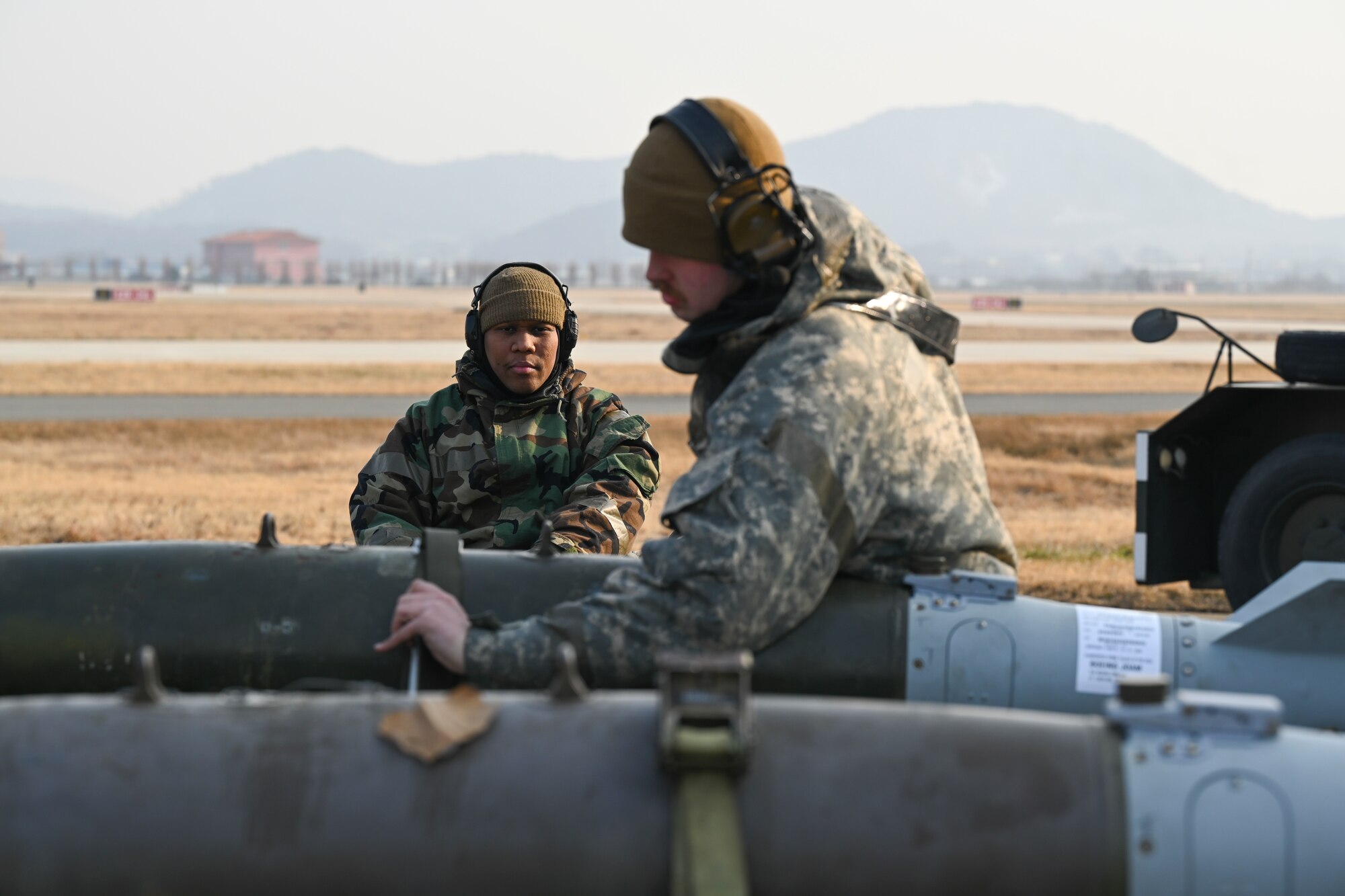 Senior Airman Frank William Jones, 35th Fighter Generation Squadron aircraft armament systems specialist, left, lifts a munition onto a tow, while Staff Sgt. Gary Beam, front, 35th FGS aircraft armament systems load crew team chief, secures it into place at Gwangju Air Base, Republic of Korea, Jan. 14, 2025.