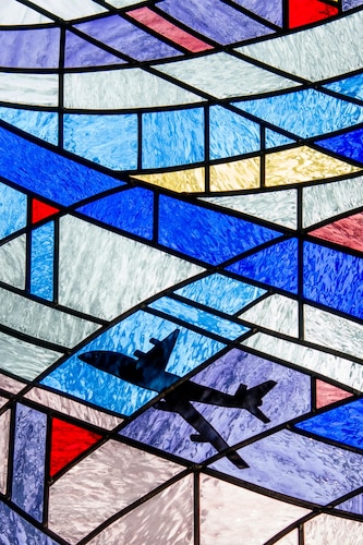 A plane flies across a sky of stained glass in a Chapel window