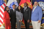 Two black women and three black men stand side by side in front of a group of flags