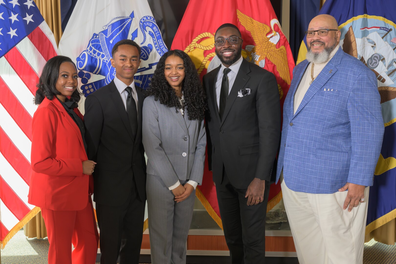 Two black women and three black men stand side by side in front of a group of flags