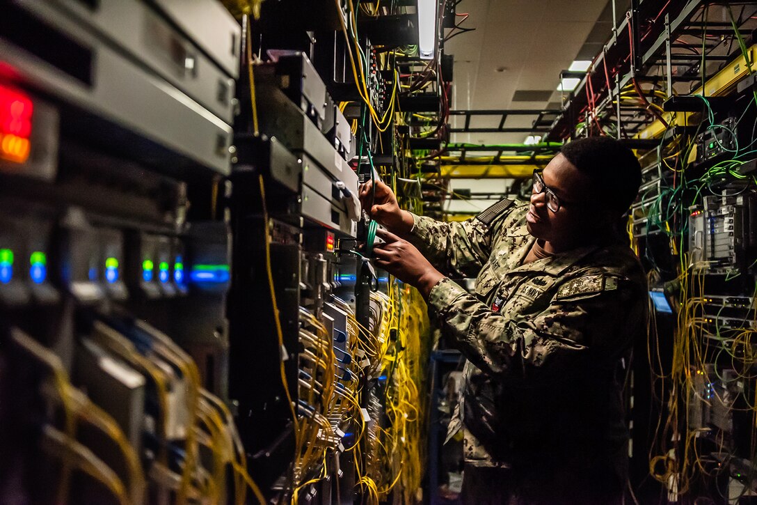 A service member inspects yellow wires in a cybersecurity lab.
