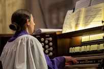 An organist plays their instrument while reading a music sheet
