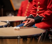 A band member waits with hands together on lap with their drum next to them