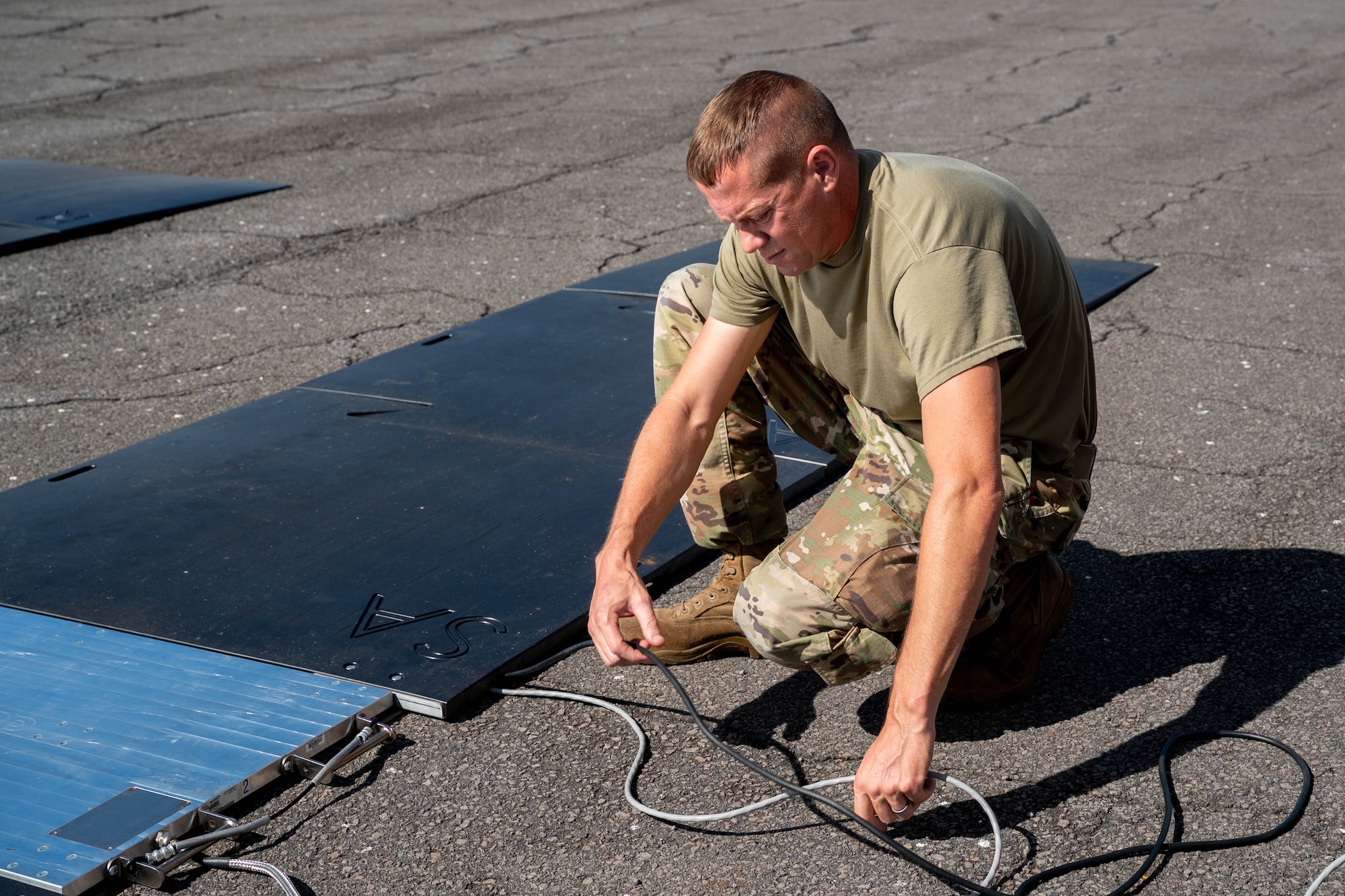 Airman moves wire around on the floor while kneeling.