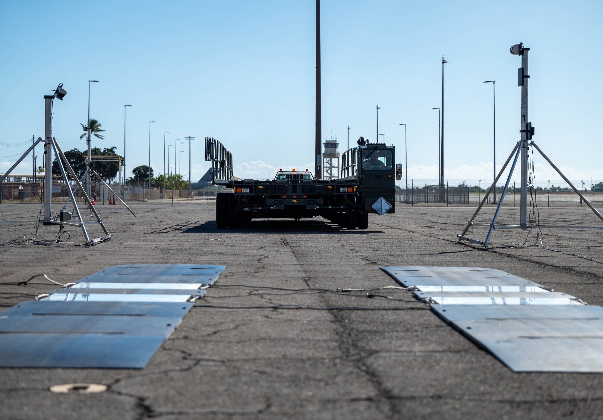 A large vehicle that carries cargo is ready to drive on top of several panels with two scanners on each side.
