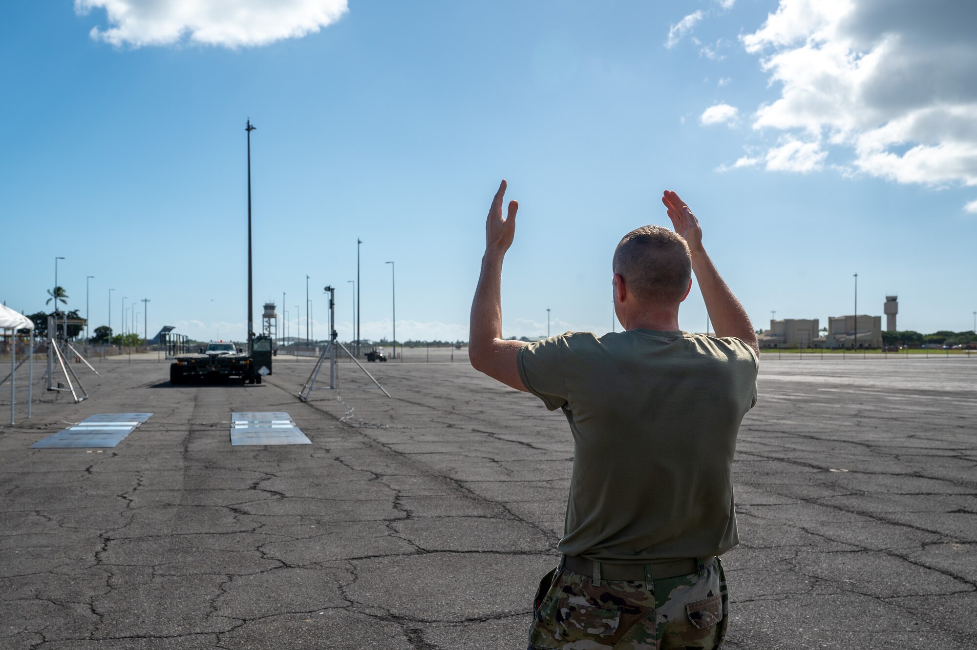 An Airman uses his arms to signal a large vehicle to move forward.