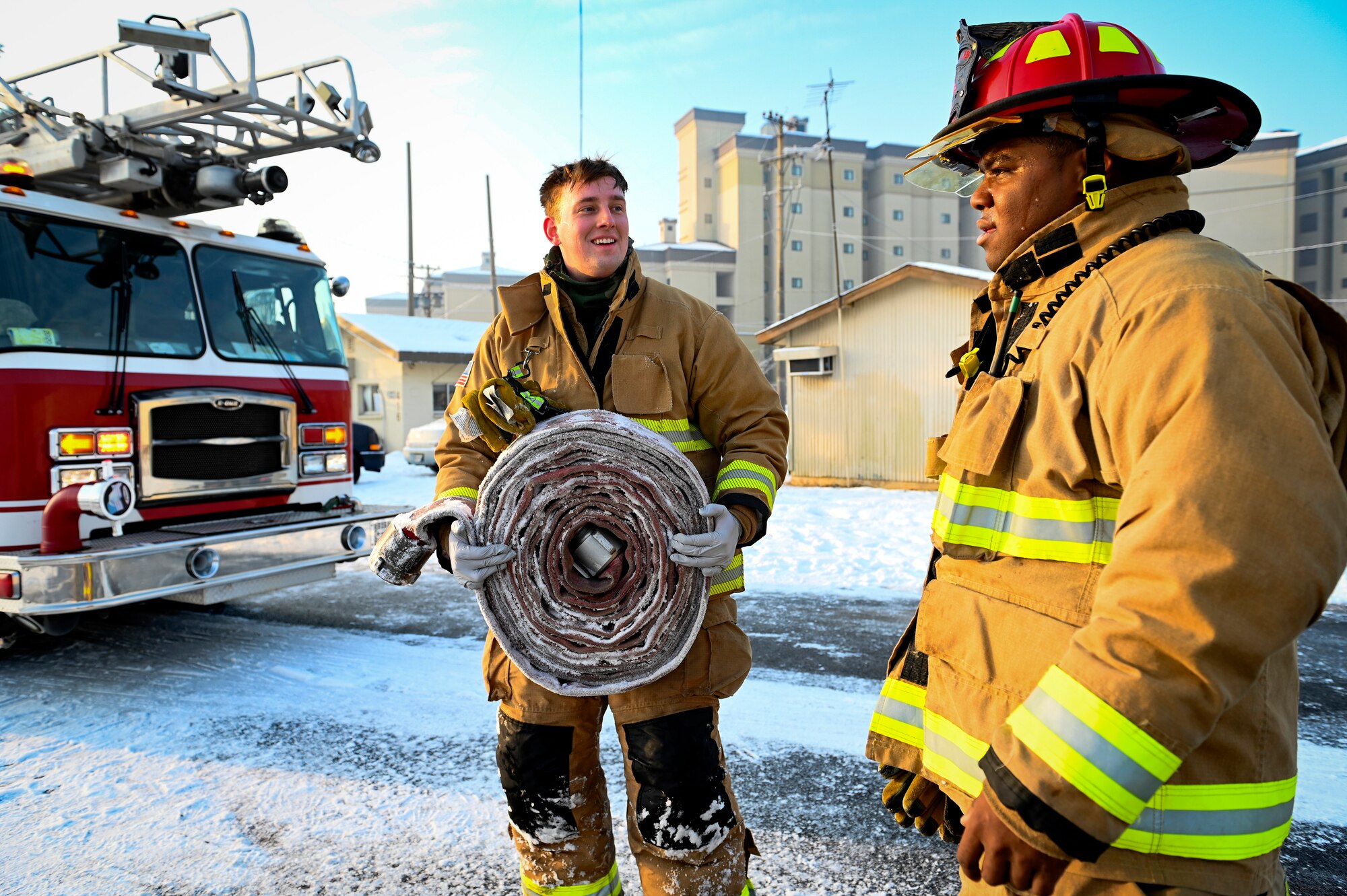 Senior Airman Benjamin McEntire, 8th Civil Engineer Squadron firefighter, holds a wrapped firehose while talking to U.S. Air Force Staff Sgt. Austin James, 8th CES firefighter, during Beverly Pack 25-1.