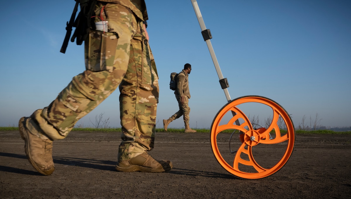 U.S. Air Force Staff Sgt. Dalton Roberts, left, 921st Contingency Response Squadron operations expeditor, takes a measurement of an unprepared flight line with Senior Airman Joel Thomas, middle, 721st CRS air traffic controller, in Rio Vista, California, Jan. 10, 2025.