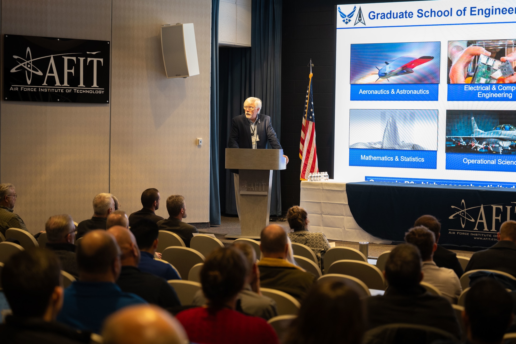 Kyle Hurst, Chief, Digital Transformation Office, gives a keynote brief to attendees for the first Digital Material Management Symposium Jan. 16, 2024, Wright-Patterson Air Force Base, Ohio. The DMM Symposium is vital to showcase student research conducted by AFIT to support various industry partners and program offices within Air Force Materiel Command. (U.S Air Force Photo by Jack Gardner.)