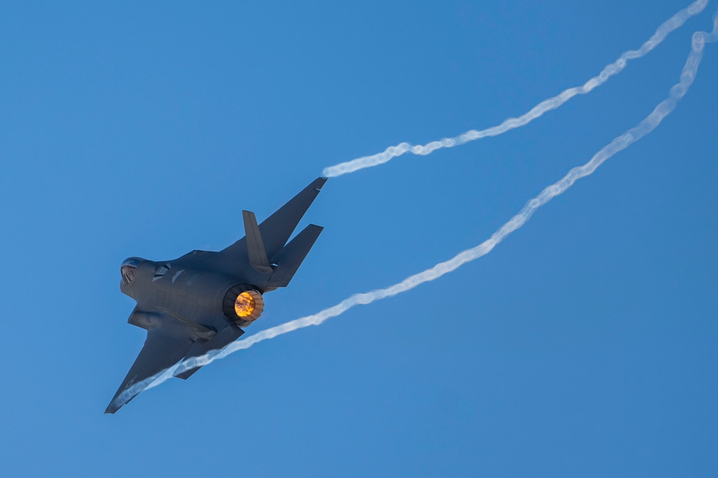 An aircraft flies to the left leaving behind two white streaks in a blue sky.