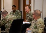 A man in a green military uniform speaks to a group of military personnel.