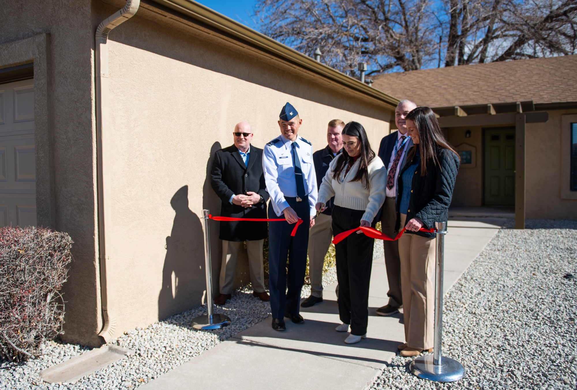 Civilians and military members cut a red ribbon in front of a house