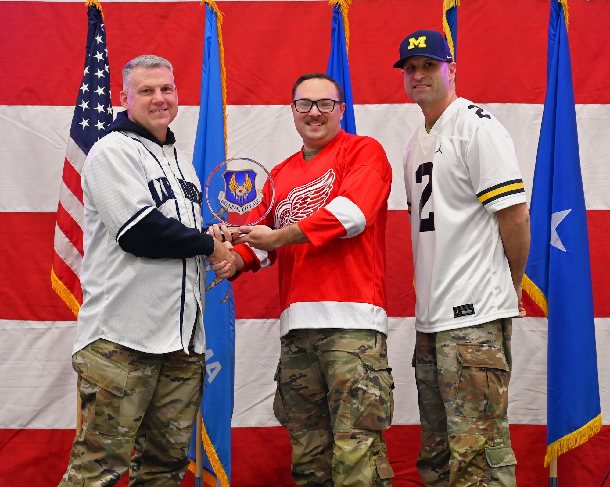Three men on a stage with middle receiving an award