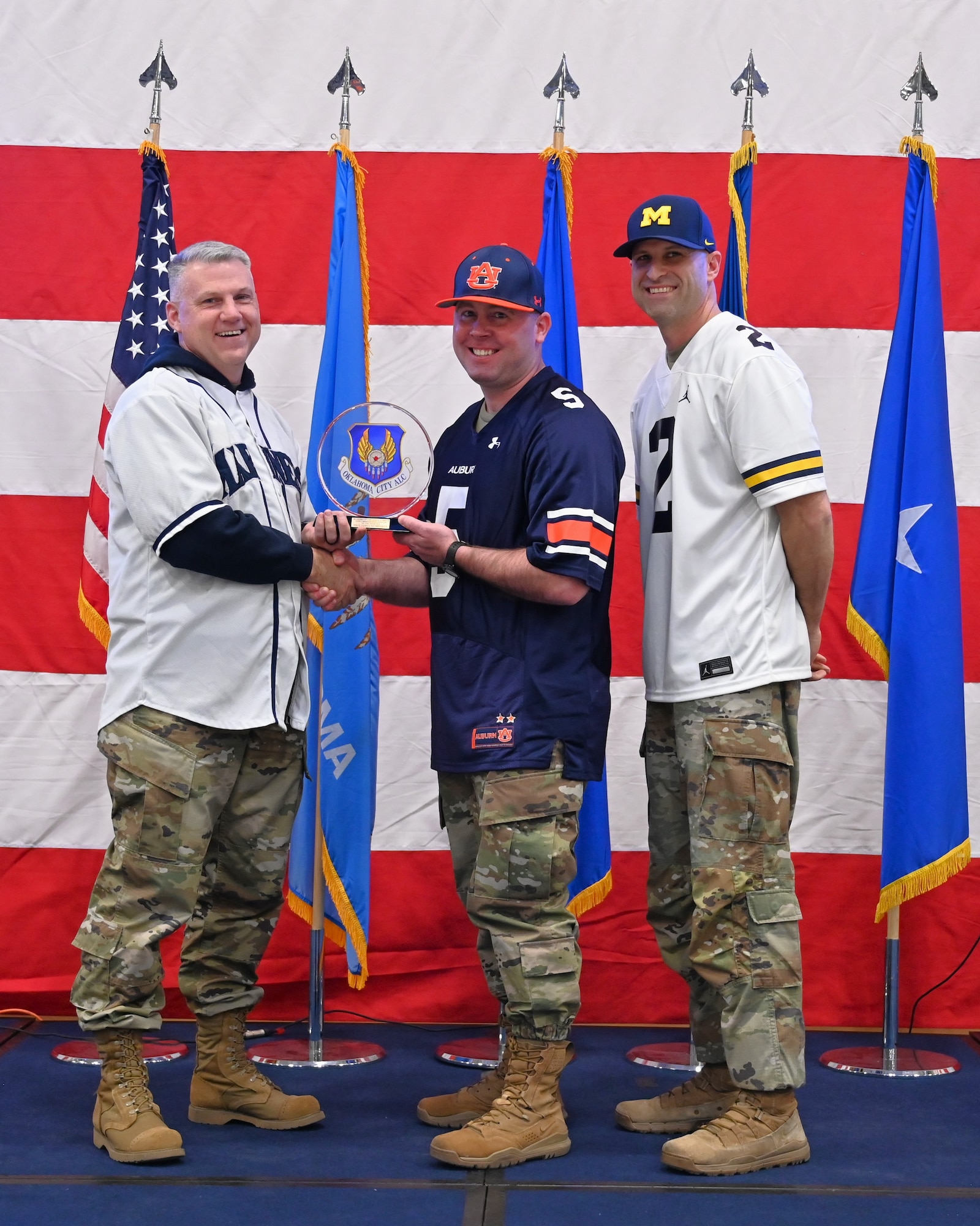 Three men on a stage with middle receiving an award