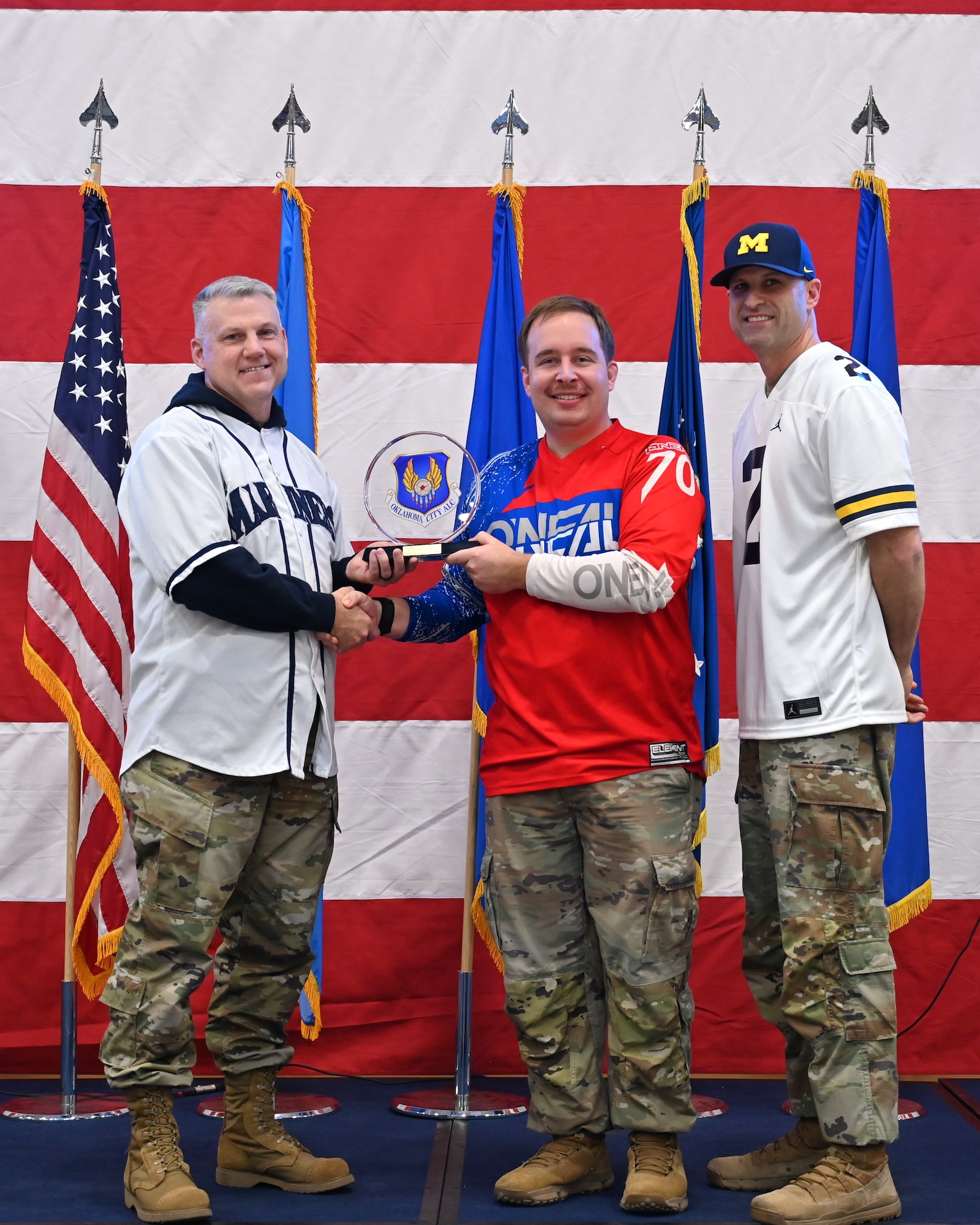 Three men on a stage with middle receiving an award