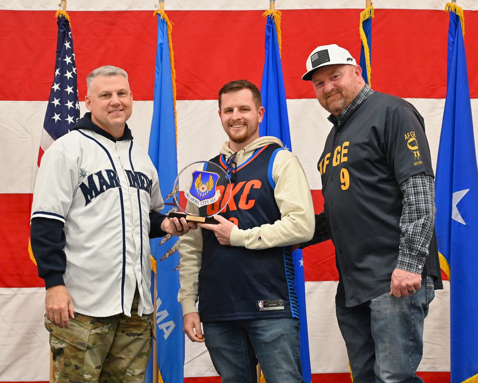 Three men on a stage with middle receiving an award