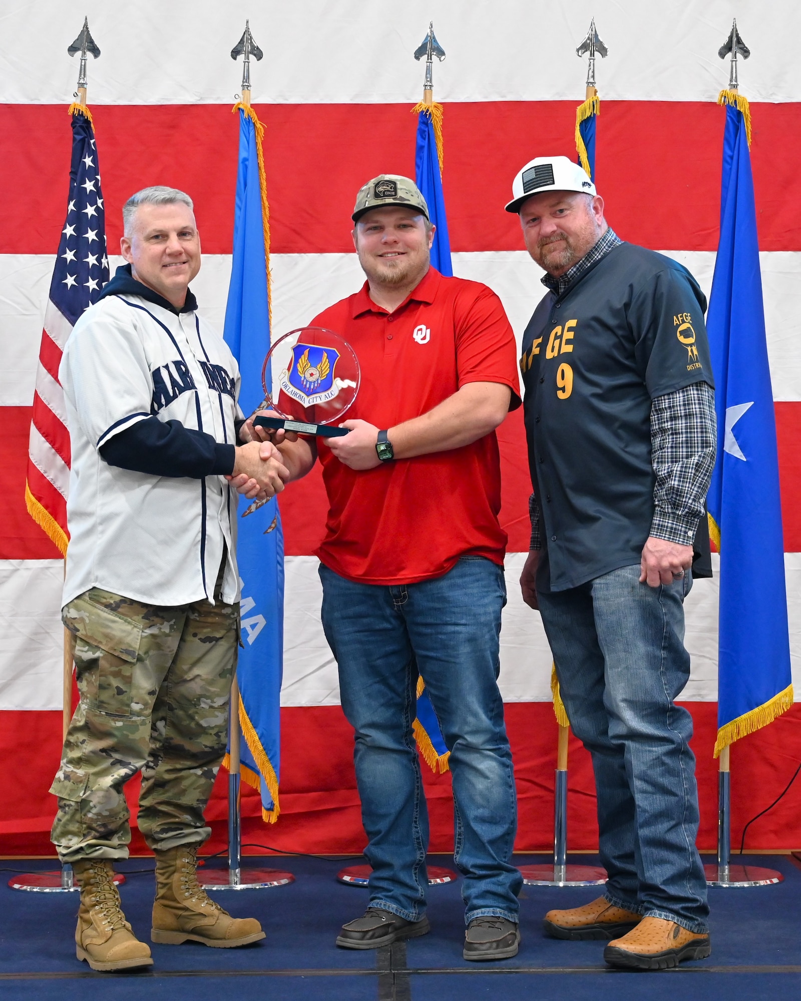 Three men on a stage with middle receiving an award