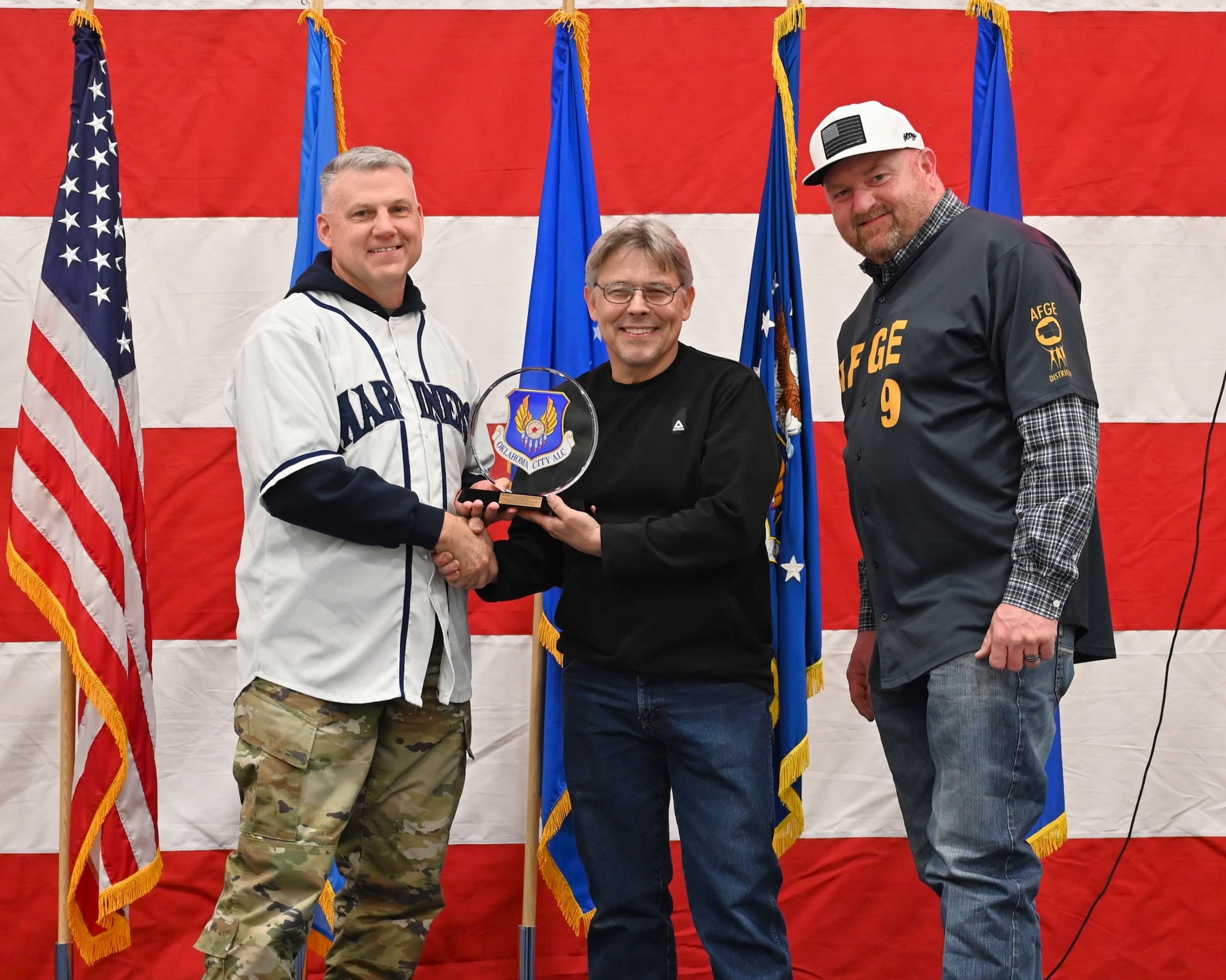 Three men on a stage with middle receiving an award