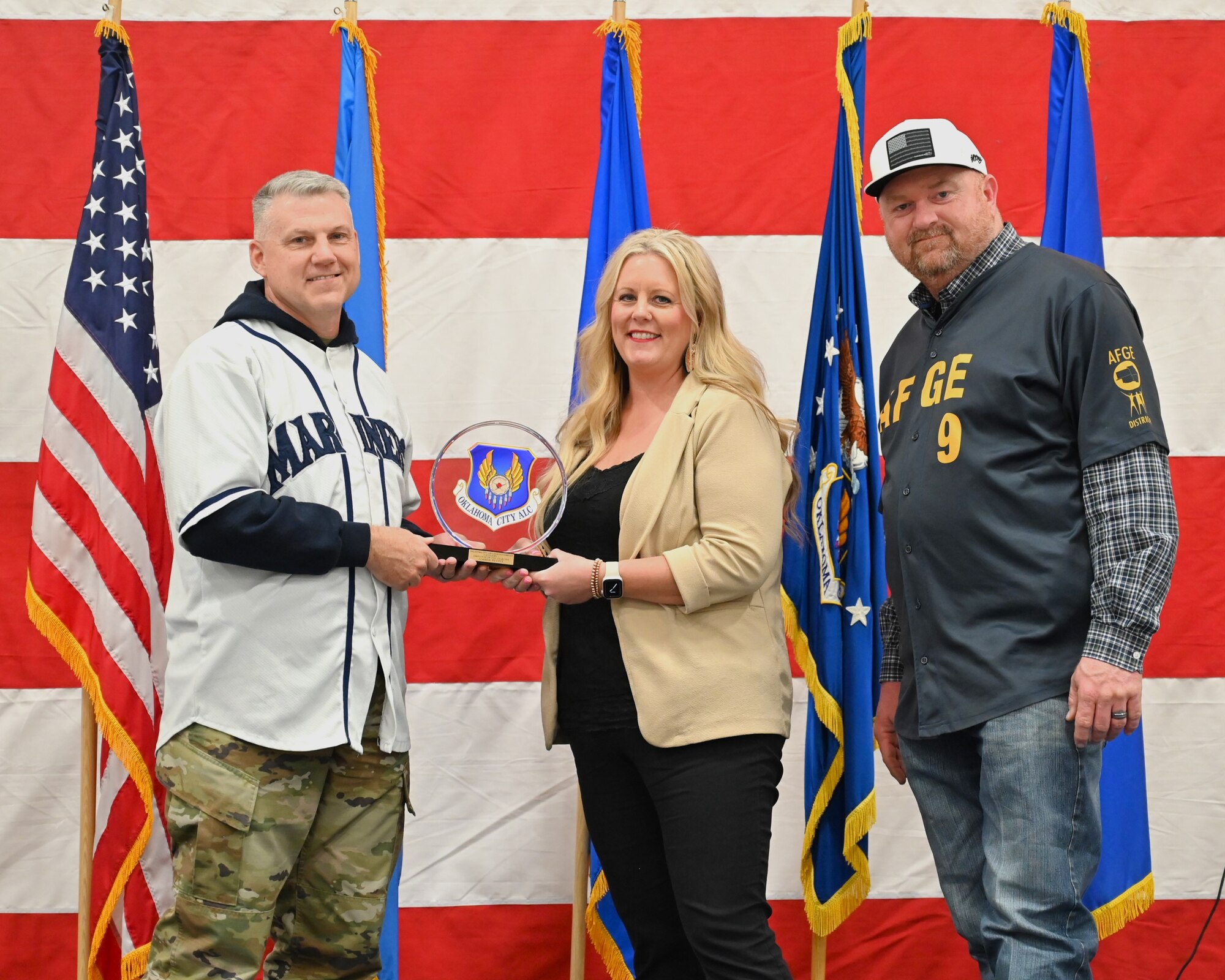 A woman in the middle of two men standing on a stage receiving an award
