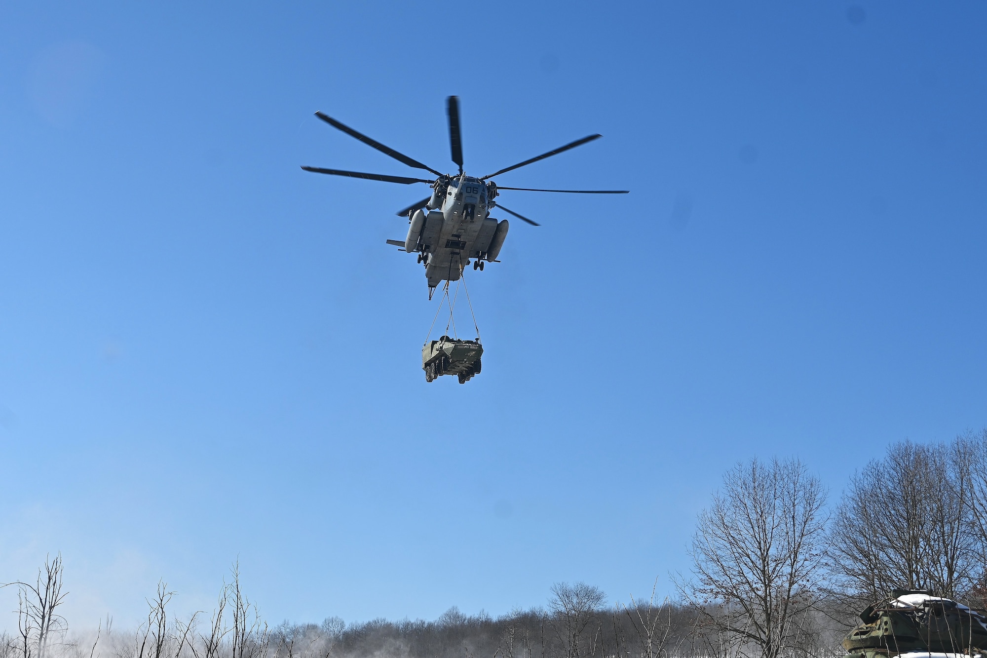 A Marine CH-53 Super Stallion helicopter from Marine Heavy Helicopter Squadron 772 out of Joint Base Maguire-Dix-Lakehurst, New Jersey, air-lifts a decommissioned Army Stryker vehicle to Fort Indiantown Gap’s impact area Jan. 22, 2025. A team of Air Force sling-load specialists from the 621st Contingency Response Group sling-loaded the Stryker to the helicopter. (Pennsylvania National Guard photo by Brad Rhen)