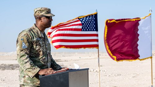 General officer speaks in front of flags at ceremony.