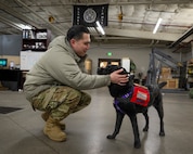A photo of an Airman petting a dog in a hangar