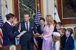 Two men hold up their right hands at ceremony while family members look on.