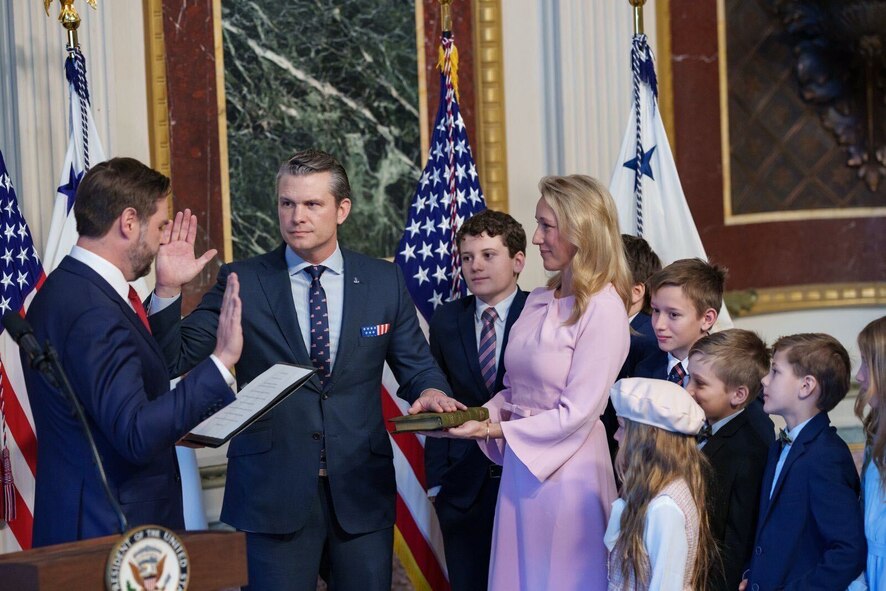 Two men hold up their right hands at ceremony while family members look on.