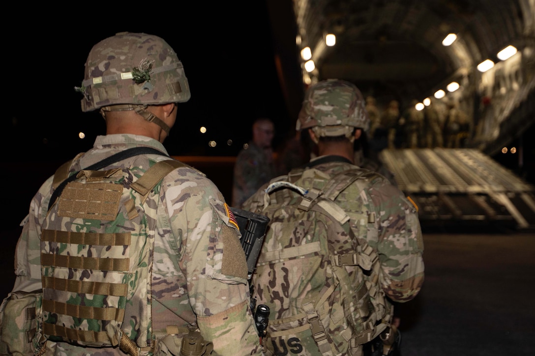 Two soldiers wearing helmets walk toward an aircraft.