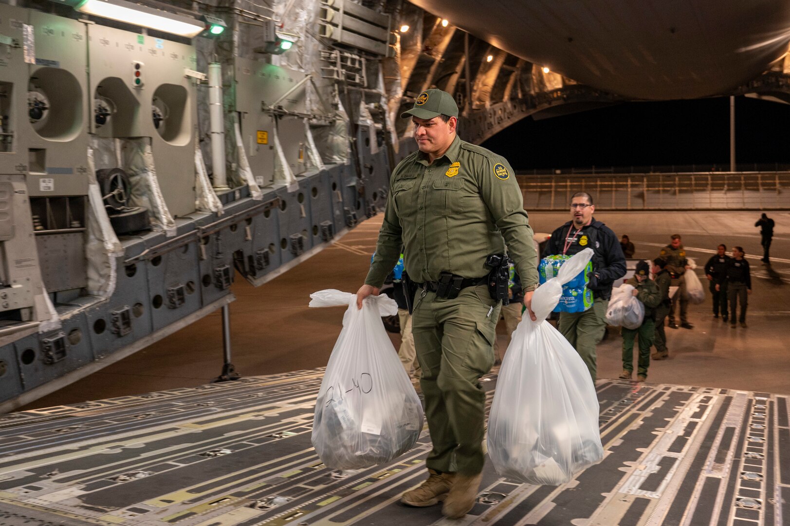 Agents load water bottles and illegal aliens' personal belongings onto an aircraft.