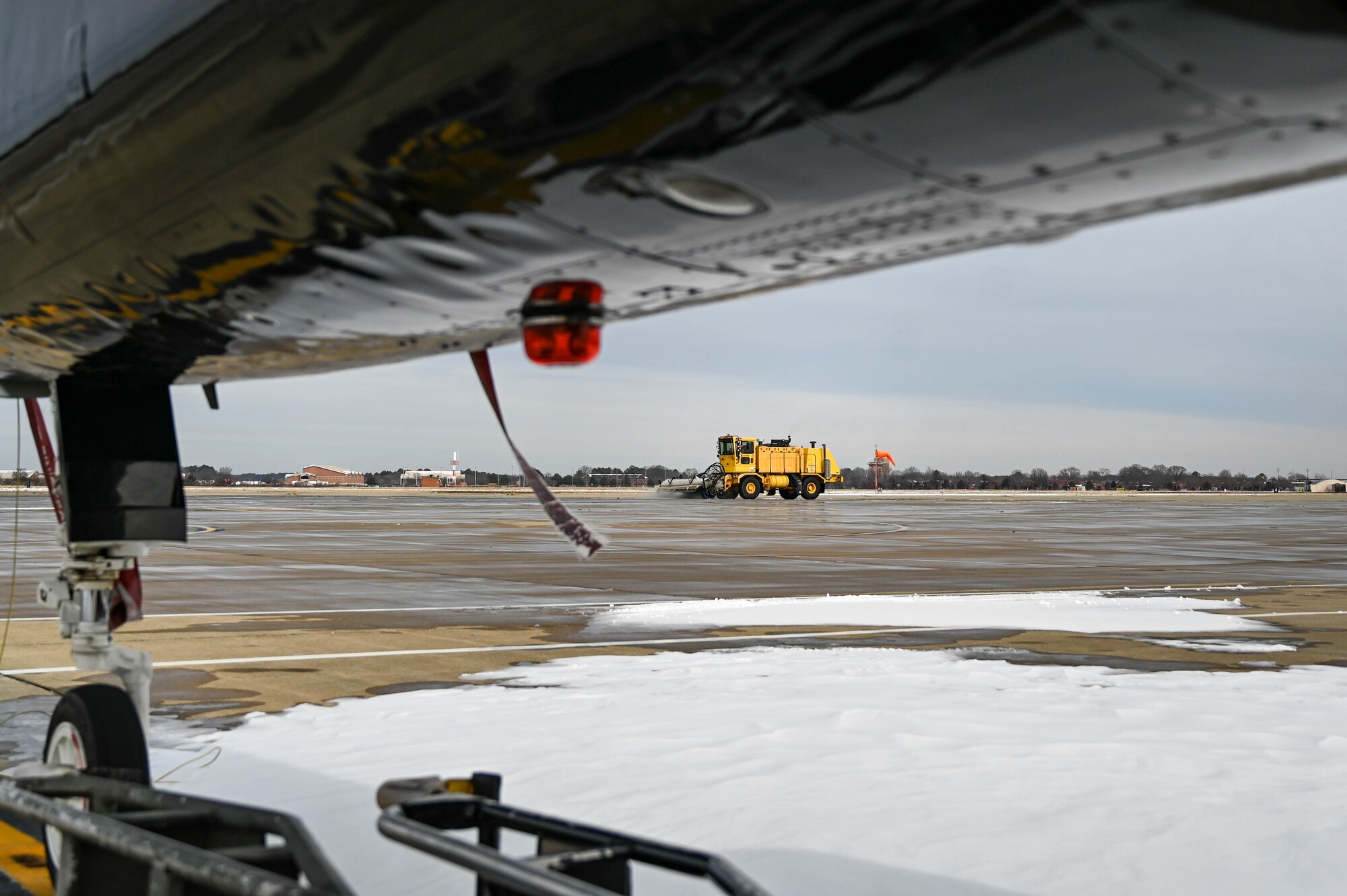 A truck with a snow broom breaking up snow and ice on a flightline
