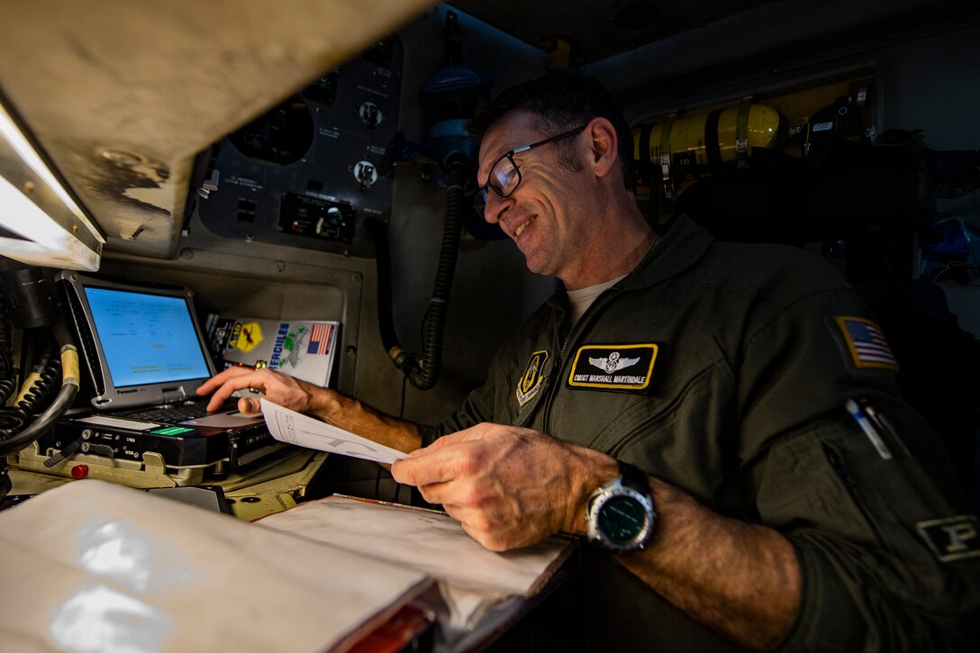 Man sits in front of a computer holding a sheet of paper with other papers scattered around him