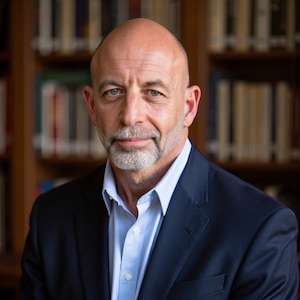 Photo of James Giordano in a suit and button down shirt, smiling in front of a bookcase.