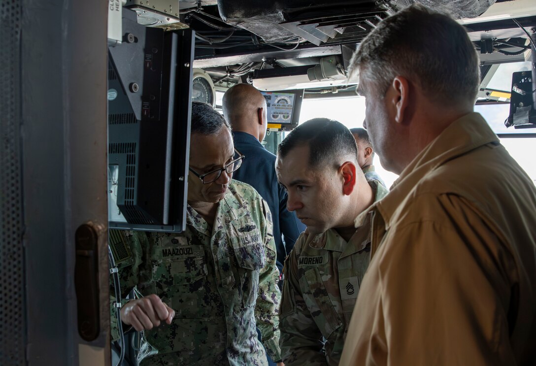 Three people look over equipment while aboard the USS Abraham Lincoln.