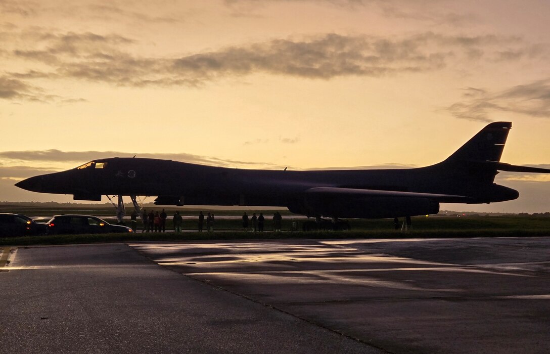 A military jet is silhouetted by a setting sun.