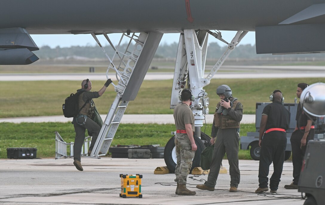 A half dozen Airmen line up to climb up a ladder into a military jet.