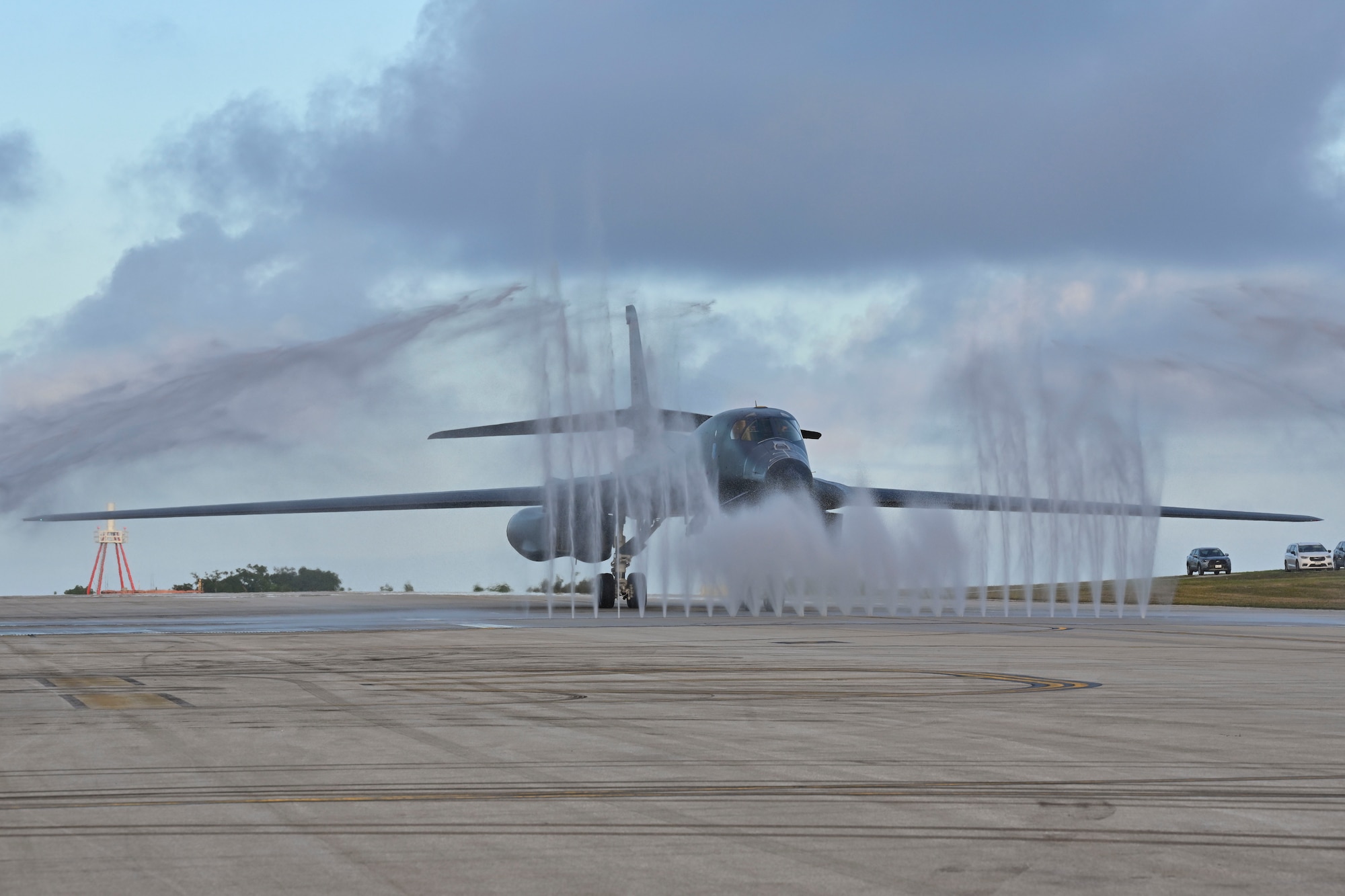 A large military jet rolls through a water jets embedded in the ground.