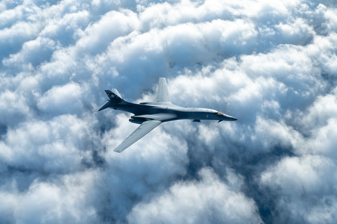 A large military jet flying above clouds.