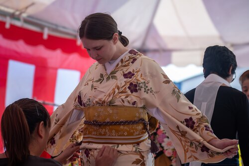 An attendee holds their arms out as they are fitted in a colorful Japanese kimono.