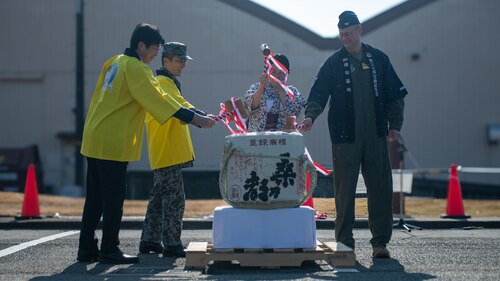 Four people swing mallets at a Japanese sake barrel.