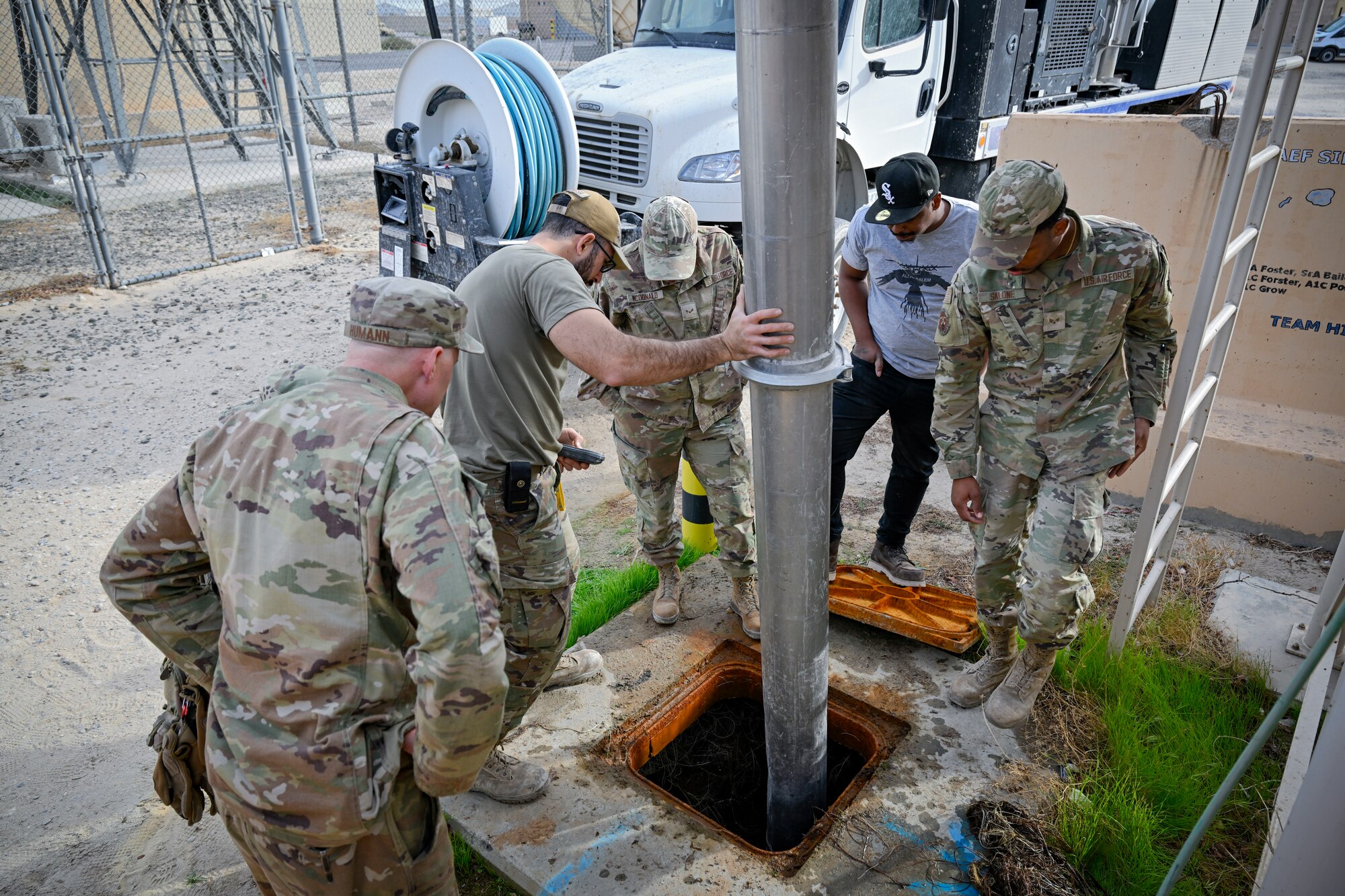 Five members watch a hydro-excavation machine in use.