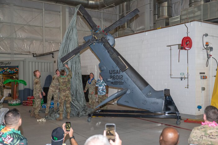 A group of men wearing military uniforms pulls a parachute off of the tail of an HH-60 Pave Hawk helicopter.