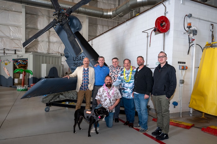 A group of men stand in front of an HH-60 Pave Hawk helicopter tail.