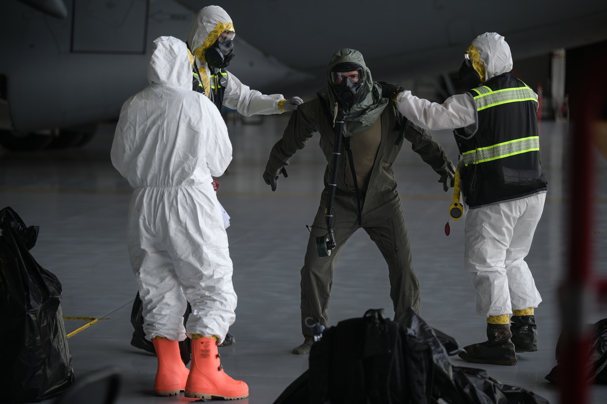 Airmen in chemical protective equipment decontaminate an aircrew member in a flight suit.