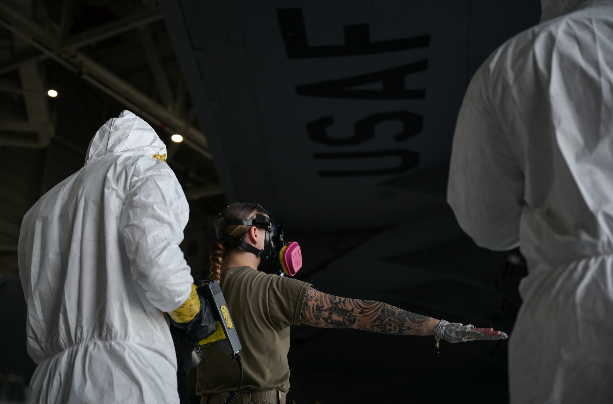 An Airman in chemical protection gear uses chemical detection equipment on another Airmen not in protective gear.